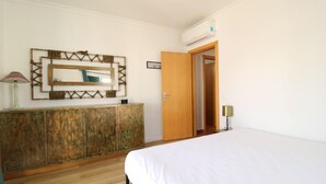 A hotel room with a wooden cabinet, a bed, a mirror, and an air conditioning unit. - Villa GrandVale (Castro Marim)