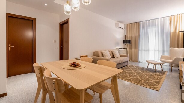 Un salon moderne avec une table à manger en bois, un canapé beige et un tapis à motifs.