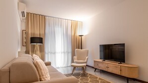 Un salon moderne avec un canapé, un fauteuil, une télévision et une lampe.