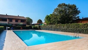 Une piscine rectangulaire avec une terrasse en bois, entourée d’une haie et d’une clôture.