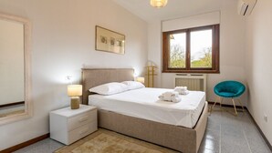 Une chambre à coucher comprenant un lit, des tables de chevet, une fenêtre, une chaise et un luminaire suspendu.