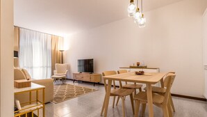 Un salon moderne comprenant un canapé, un téléviseur, une table à manger avec des chaises et un lustre.