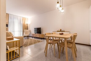 Ein modernes Wohnzimmer mit einer Couch, einem Fernseher, einem Esstisch mit Stühlen und einer Pendelleuchte.