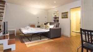 Un dormitorio moderno con cama, un sofá gris, un televisor y una estantería.