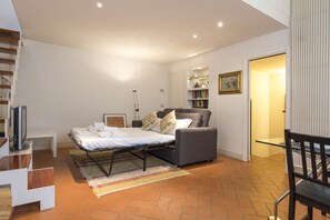 A modern bedroom with a bed, a grey sofa, a TV, and a bookshelf. - Santa Croce Cozy Duplex (Firenze)