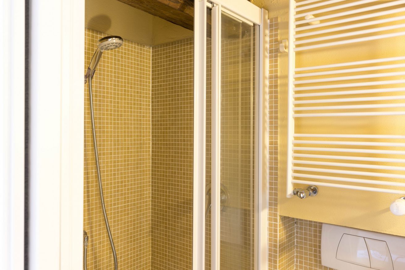 Une douche avec une porte en verre, un mur carrelé et un radiateur blanc.