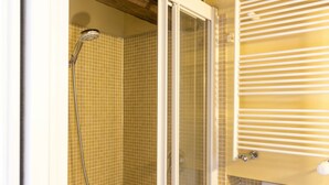 Una ducha con puerta de cristal, pared de azulejos y radiador blanco.
