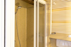A shower with a glass door, a tiled wall, and a white radiator. - Santa Croce Cozy Duplex (Firenze)
