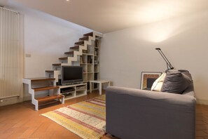 A living room with a grey sofa, a flat-screen TV, a staircase with bookshelves, and a patterned rug. - Santa Croce Cozy Duplex (Firenze)