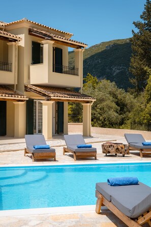 Un edificio de dos plantas con piscina, mobiliario exterior y un paisaje montañoso al fondo.