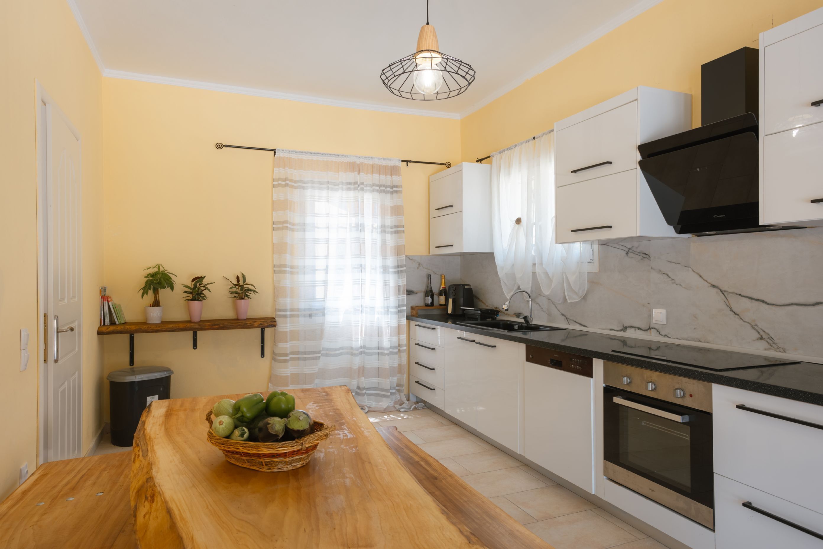 Una cocina moderna con armarios blancos, encimera de mármol y una mesa de comedor de madera con una cesta de fruta.