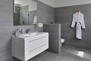 A modern bathroom with a large mirror, a white vanity, a round mirror, and a white robe hanging on the wall. - Penthouse Apt Historic Charm Incredible Views (Cape Town)