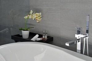 A modern bathroom with a white bathtub, a black vanity with a potted orchid, and a chrome faucet. - Penthouse Apt Historic Charm Incredible Views (Cape Town)