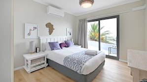 A modern bedroom with a large bed, a bedside table, a lamp, and a view of the outdoors. - Spacious Family Camps Bay Escape Spectacular Views Pool Garden (Cape Town)