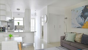 A modern kitchen with white cabinets, a dining area with a white table and chairs, and a living room with a gray sofa and a painting. - Charming Central Sea Point Haven 50m to Ocean (Cape Town)