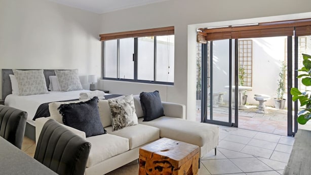 A modern living room with a sofa, a coffee table, and a bed with patterned pillows. - Modern Sea Point Oasis Garden Pool BBQ Gym (Cape Town)