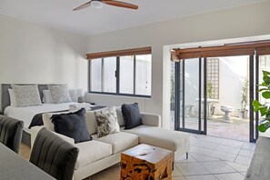 A modern living room with a sofa, a coffee table, and a bed with patterned pillows. - Modern Sea Point Oasis Garden Pool BBQ Gym (Cape Town)