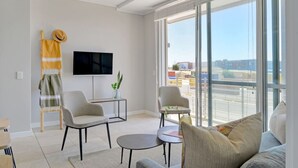A modern living room with a flat-screen TV, two armchairs, a sofa, and a small coffee table. - Modern 1-bed V A Waterfront Canal Harbor Views (Cape Town)