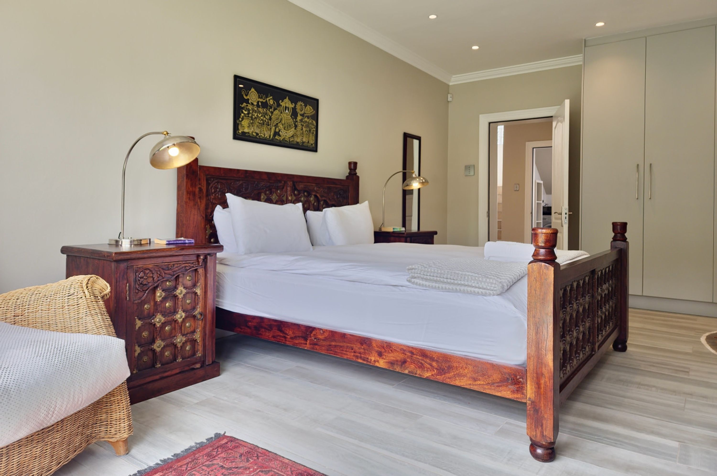Een slaapkamer met een houten bed, twee nachtkastjes met lampen, een rieten stoel en een rood vloerkleed.