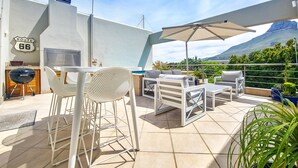 Een terras buiten met een barbecue, witte meubels en uitzicht op een berg.