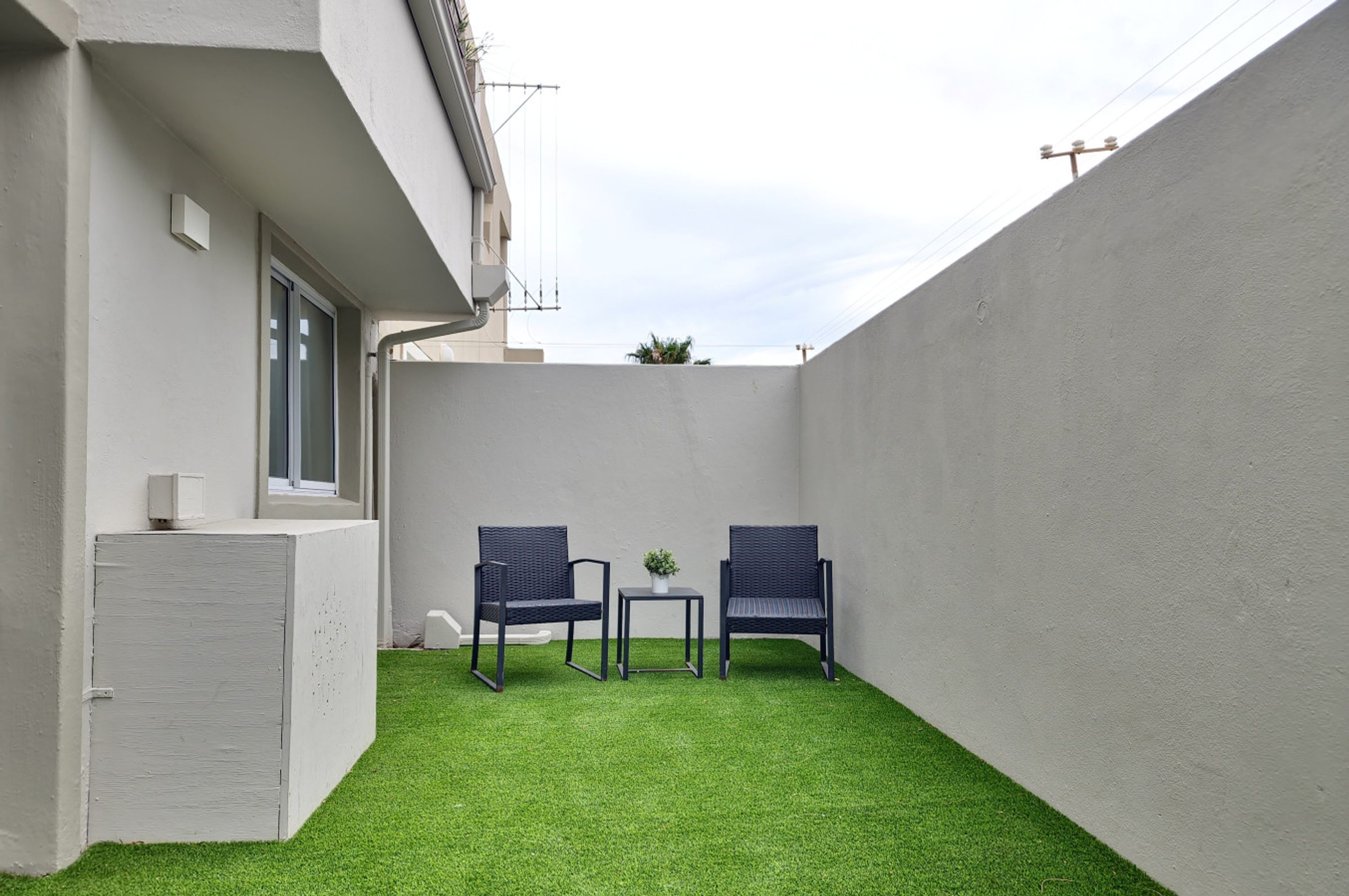 A small outdoor area with artificial green turf, two wicker chairs, a small table, and a white cabinet.