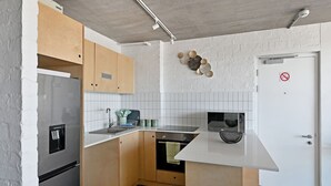 Una cucina compatta con frigorifero, fornello, microonde e lavello. Si nota una porta bianca con il cartello 'no smoking' e un piccolo ripiano con oggetti decorativi.