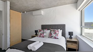 Una moderna camera d'albergo con un letto grande, cuscini floreali, una lampada da comodino e una finestra vista esterna.