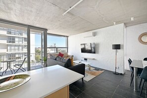 Ein modernes Wohnzimmer mit großem Fernseher, einer Couch, einem Essbereich und einem Balkon mit Blick auf die Stadt.