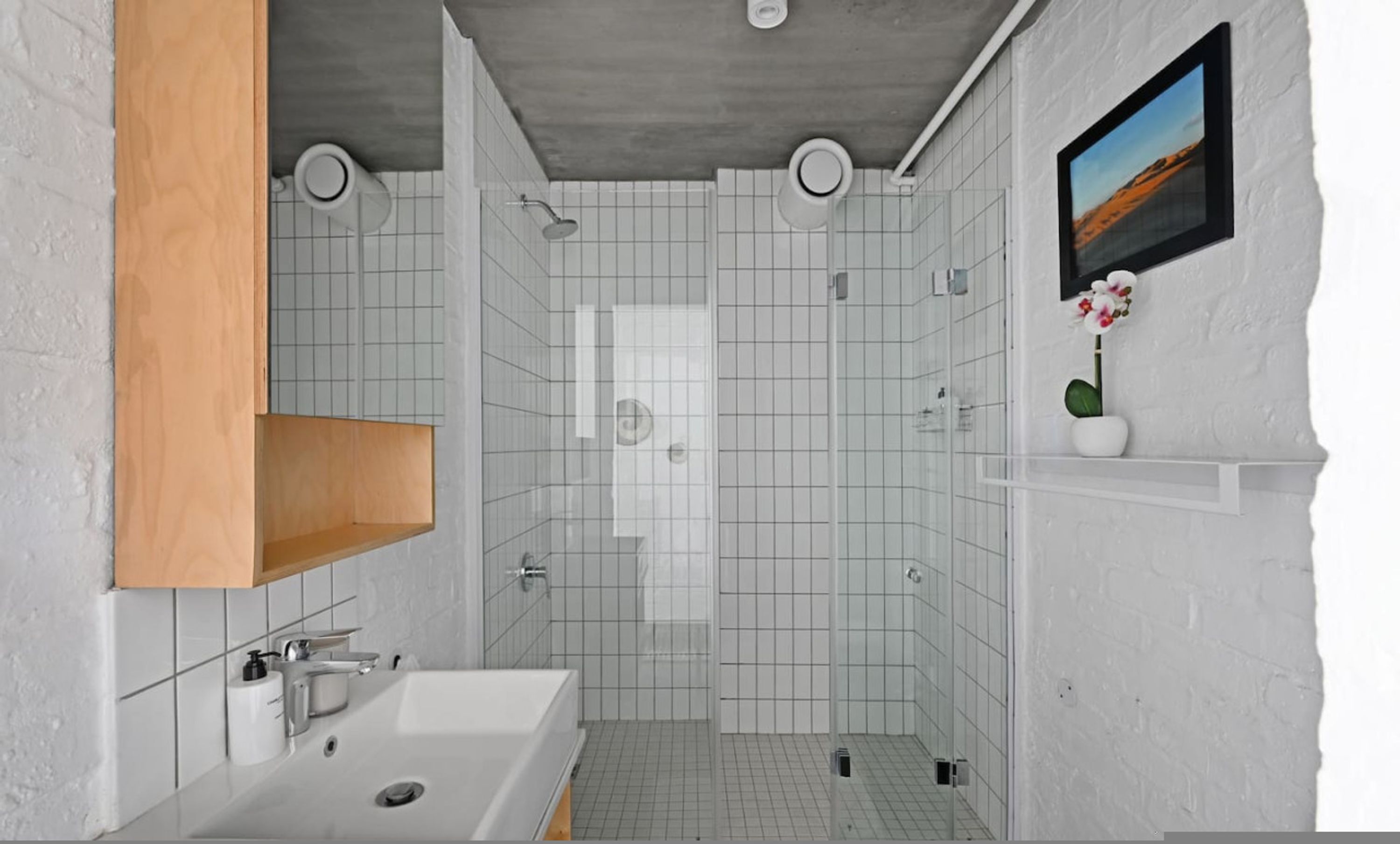 Un baño moderno con bañera, ducha e inodoro. Hay un estante de madera y un cuadro en la pared.