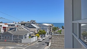 A residential street with houses, a clear blue sky, and the ocean in the background. - Modern Living Mountain Ocean View 100m to Beach (Cape Town)
