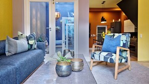 Ein modernes Wohnzimmer mit Sofa, Sessel und Couchtisch, mit dekorativen Vasen und Blick durch eine Glastür auf einen Außenbereich.
