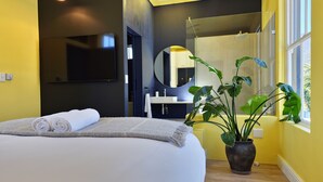 Ein modernes Schlafzimmer mit einem Bett, einem großen Spiegel, einem Fernseher und einer Topfpflanze.