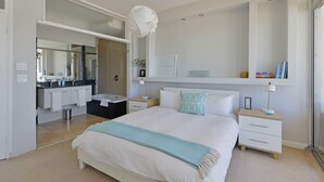 A modern bedroom with a large bed, bedside tables, a nightstand, a mirror, and a built-in shelf with books. - Top-floor 2-bed Beachfront Sunny Camps Bay Views (Cape Town)