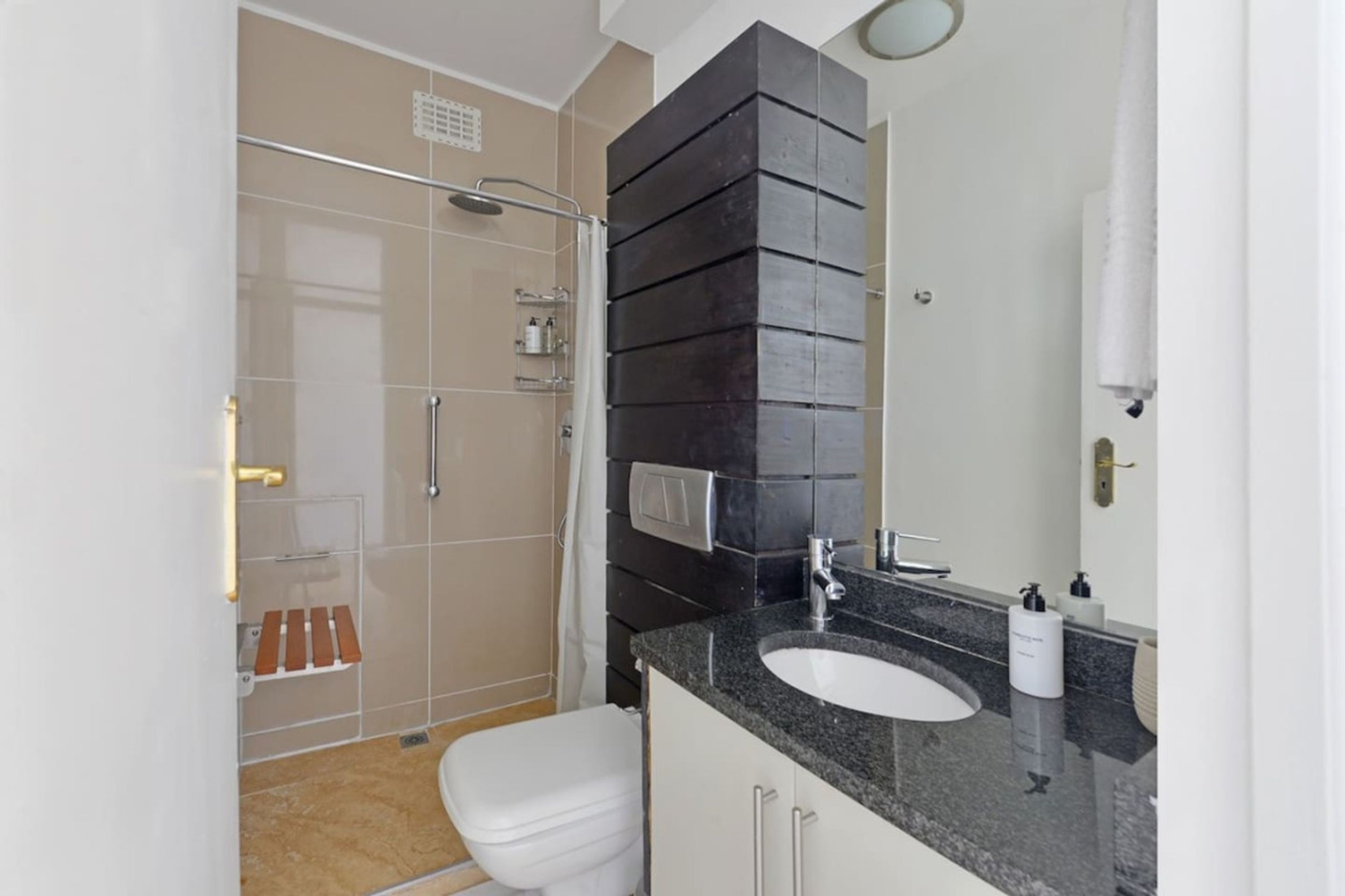 A modern bathroom with a glass shower enclosure, a white toilet, a granite countertop sink, and a large mirror.