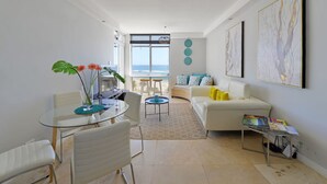 A modern living room with a glass dining table, white sofas, and a view of the ocean. - Top-floor 2-bed Beachfront Sunny Camps Bay Views (Cape Town)