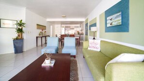 Un salon moderne avec un canapé, des fauteuils et une table basse. On aperçoit à l’arrière-plan un coin repas avec une table et des chaises.
