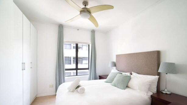 Une chambre d’hôtel avec un lit, un ventilateur de plafond, une fenêtre avec des rideaux et une table de chevet avec une lampe.
