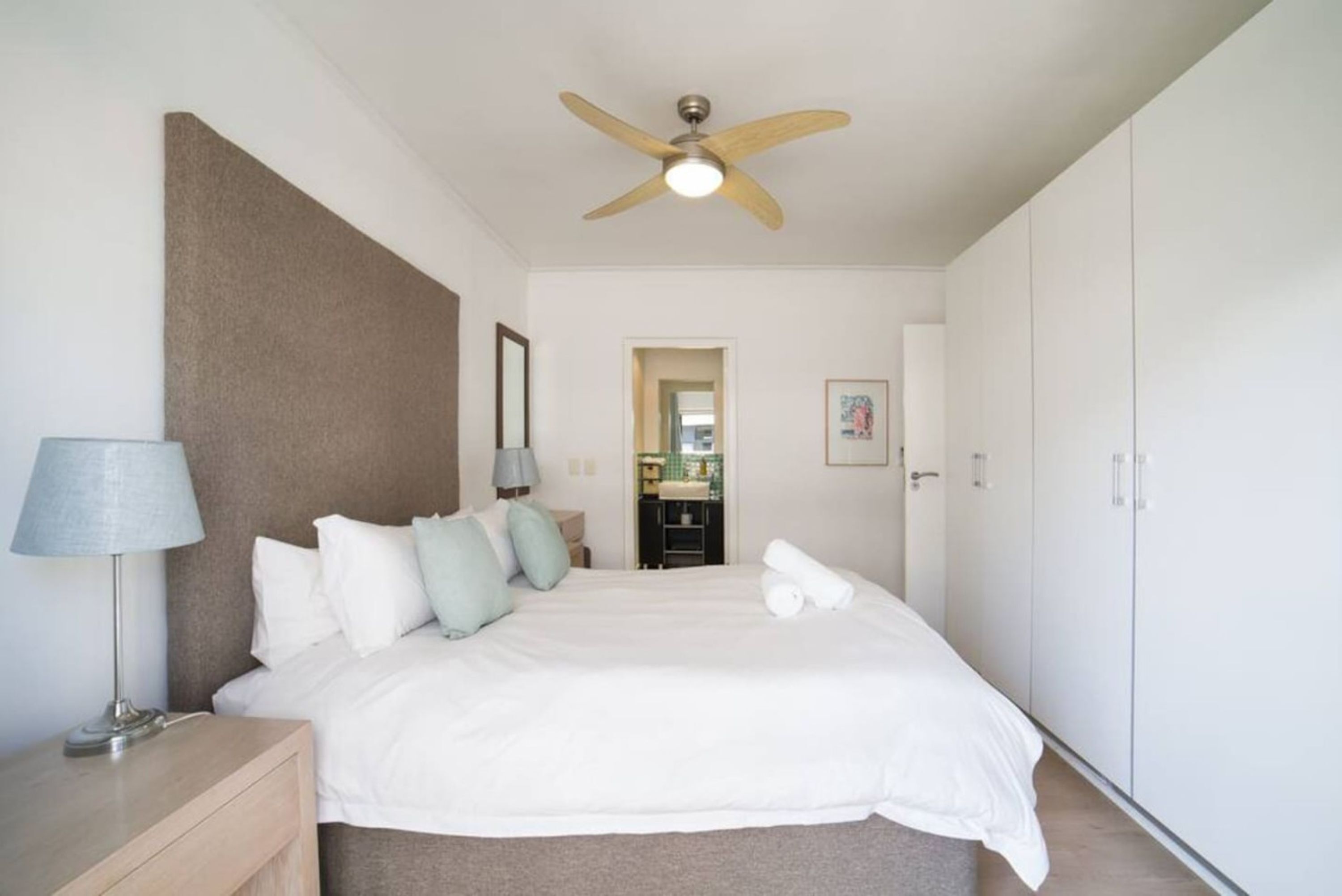 A bedroom with a bed, a ceiling fan, a nightstand, a lamp, a mirror, and a wardrobe.