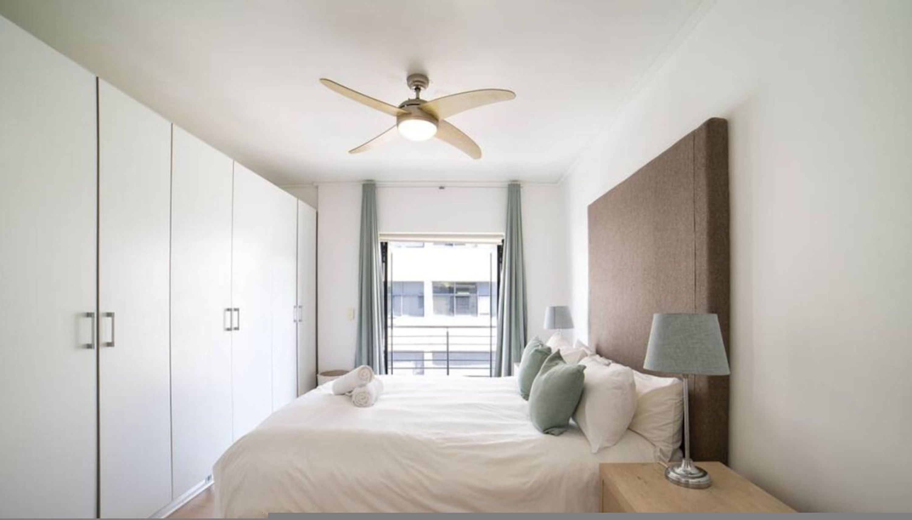 Een hotelkamer met een bed, nachtkastje, lamp, plafondventilator en uitzicht.