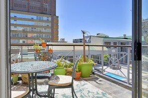 En balkon med et bord og stole, blomsterkrukker og udsigt til bygninger.
