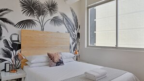 A neatly made bed with white linens, a patterned throw blanket, and a folded towel on the side. - Refined City Living Sunny Pool Gym Facilities (Cape Town)