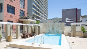 A rooftop pool area with a rectangular pool, lounge chairs, and a stone wall. - Refined City Living Sunny Pool Gym Facilities (Cape Town)