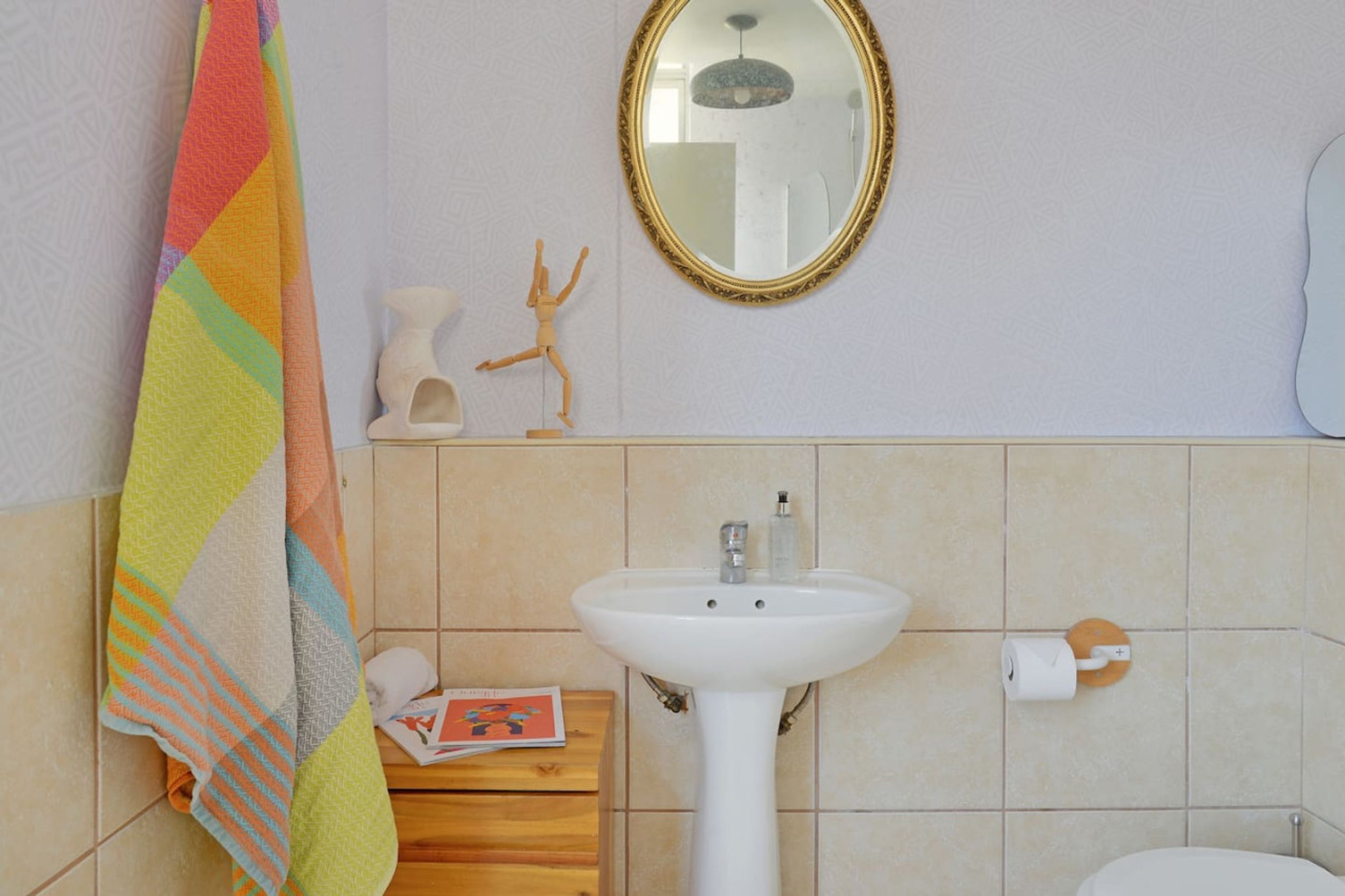 A bathroom with a white sink, a mirror, a towel rack, a toilet paper holder, and a small wooden cabinet.