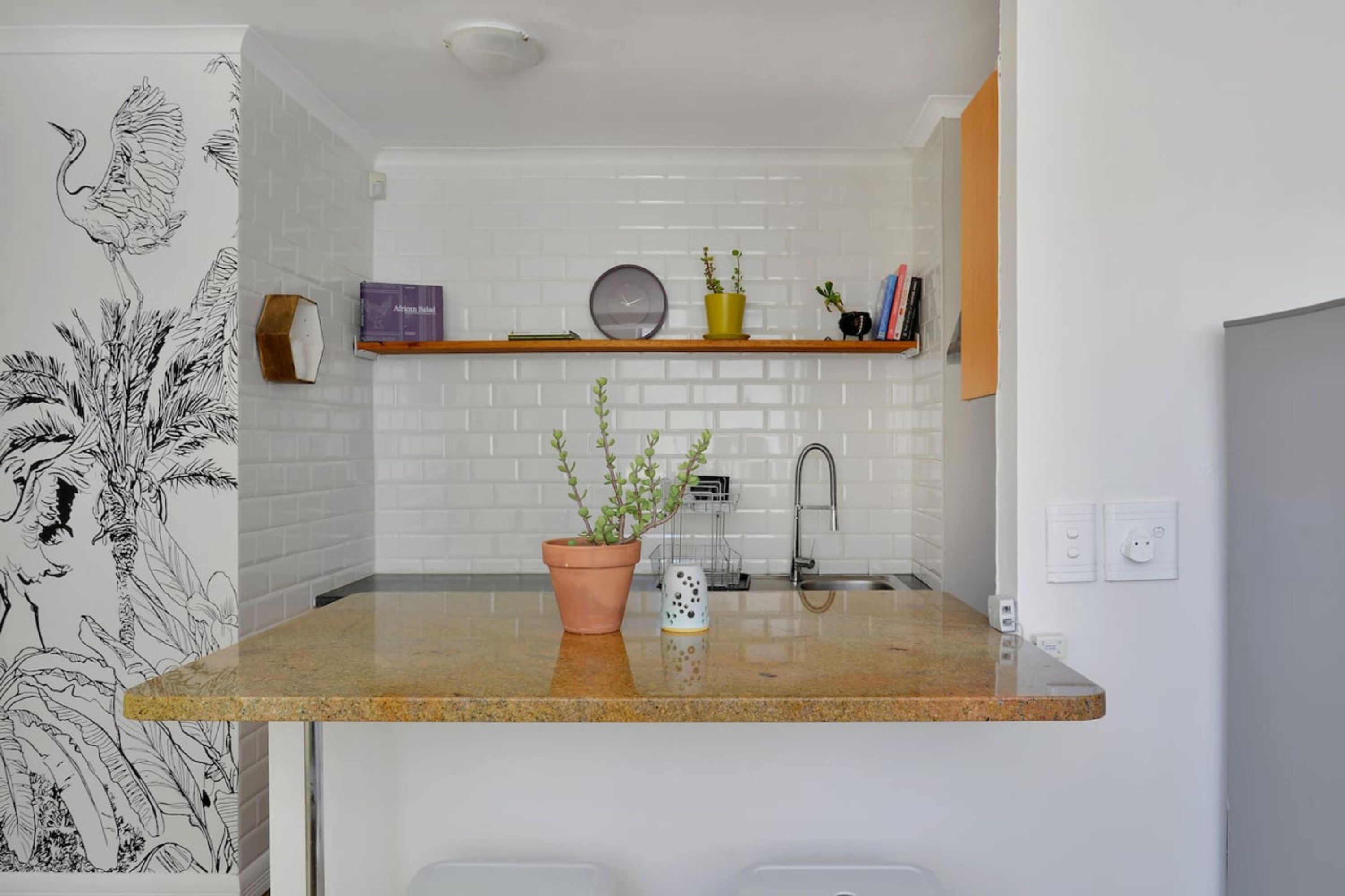 Een keuken met een witte metrotegel achterwand, een granieten aanrecht, een spoelbak en een plank met decoratieve objecten.