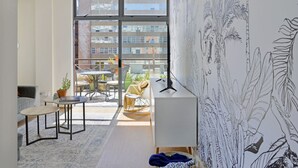 A modern living room with a large window, a white desk, a sofa, and a small table. - Refined City Living Sunny Pool Gym Facilities (Cape Town)