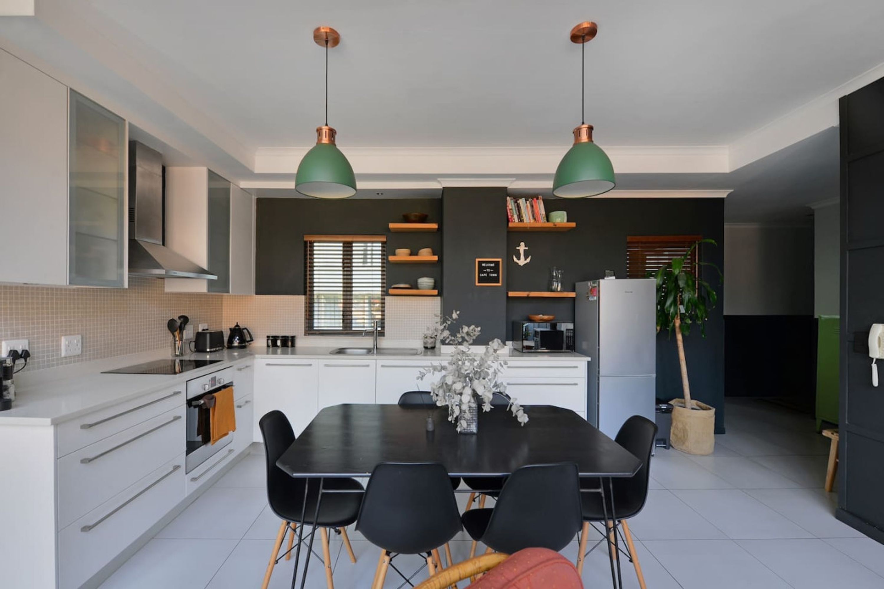 Een moderne keuken met witte kasten, een zwarte eettafel en twee hanglampen.