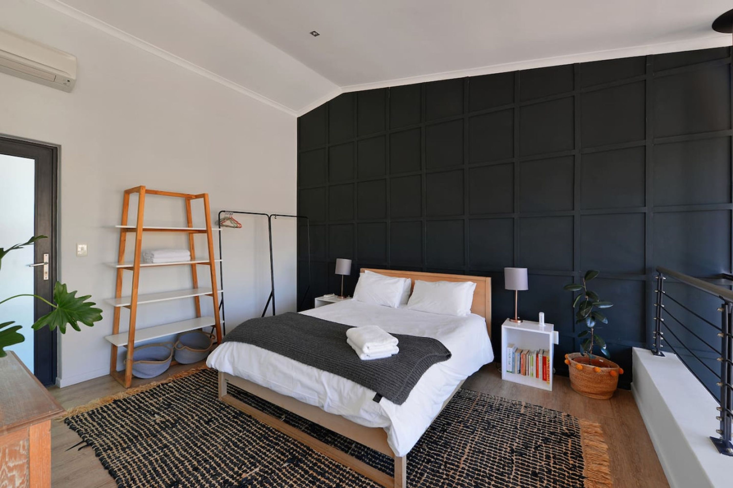 A modern bedroom with a large bed, a wooden ladder, a bookshelf, and a dark wall paneling.