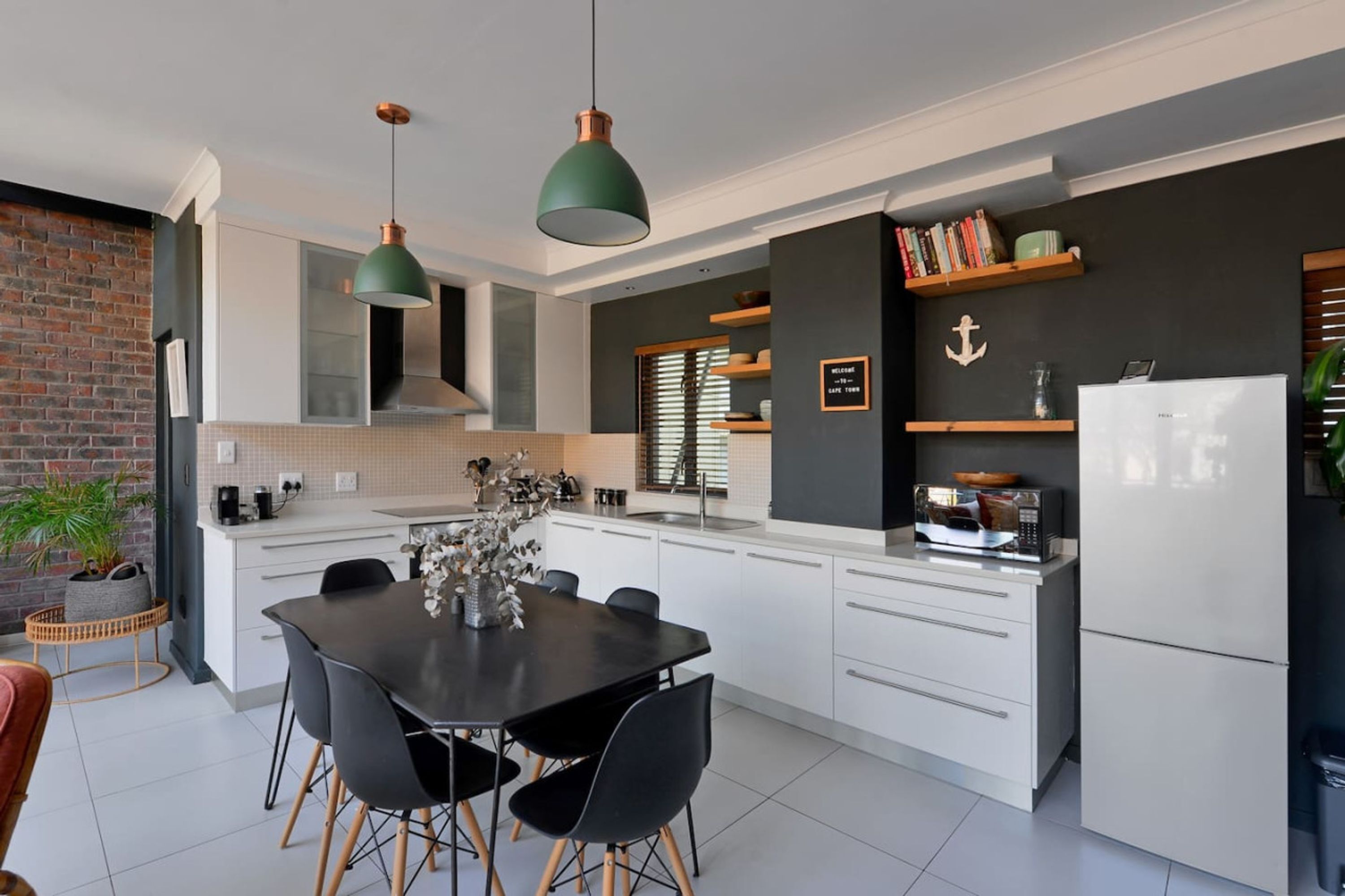 A modern kitchen with white cabinetry, a black dining table, and pendant lights.