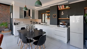 Une cuisine moderne avec des meubles blancs, une table à manger noire et des luminaires suspendus.