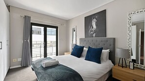 A modern hotel room with a large bed, a grey headboard, and a balcony with grey curtains. - Modern 3-bed Apt Designer Touch Mountain Views (Cape Town)